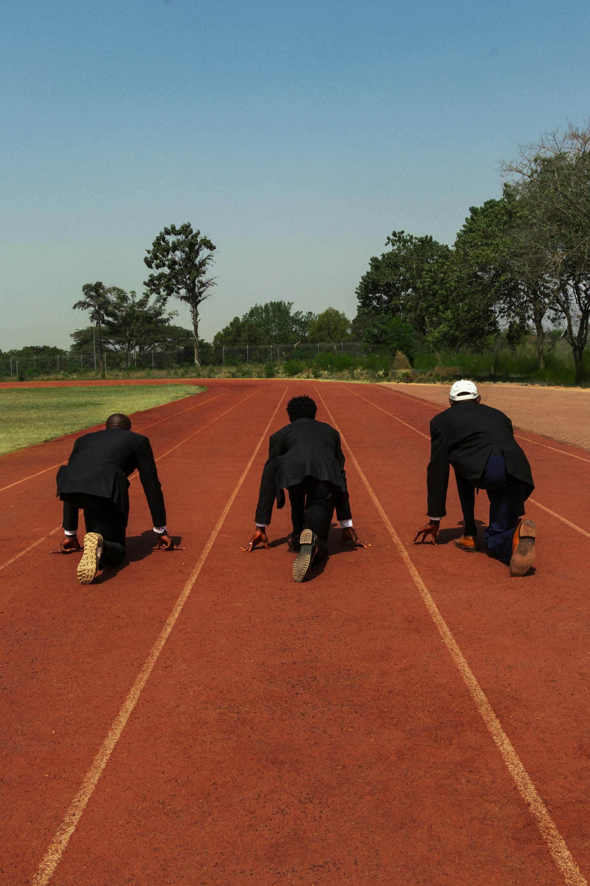 Three businessmen in suits crouched at the starting line on an outdoor running track