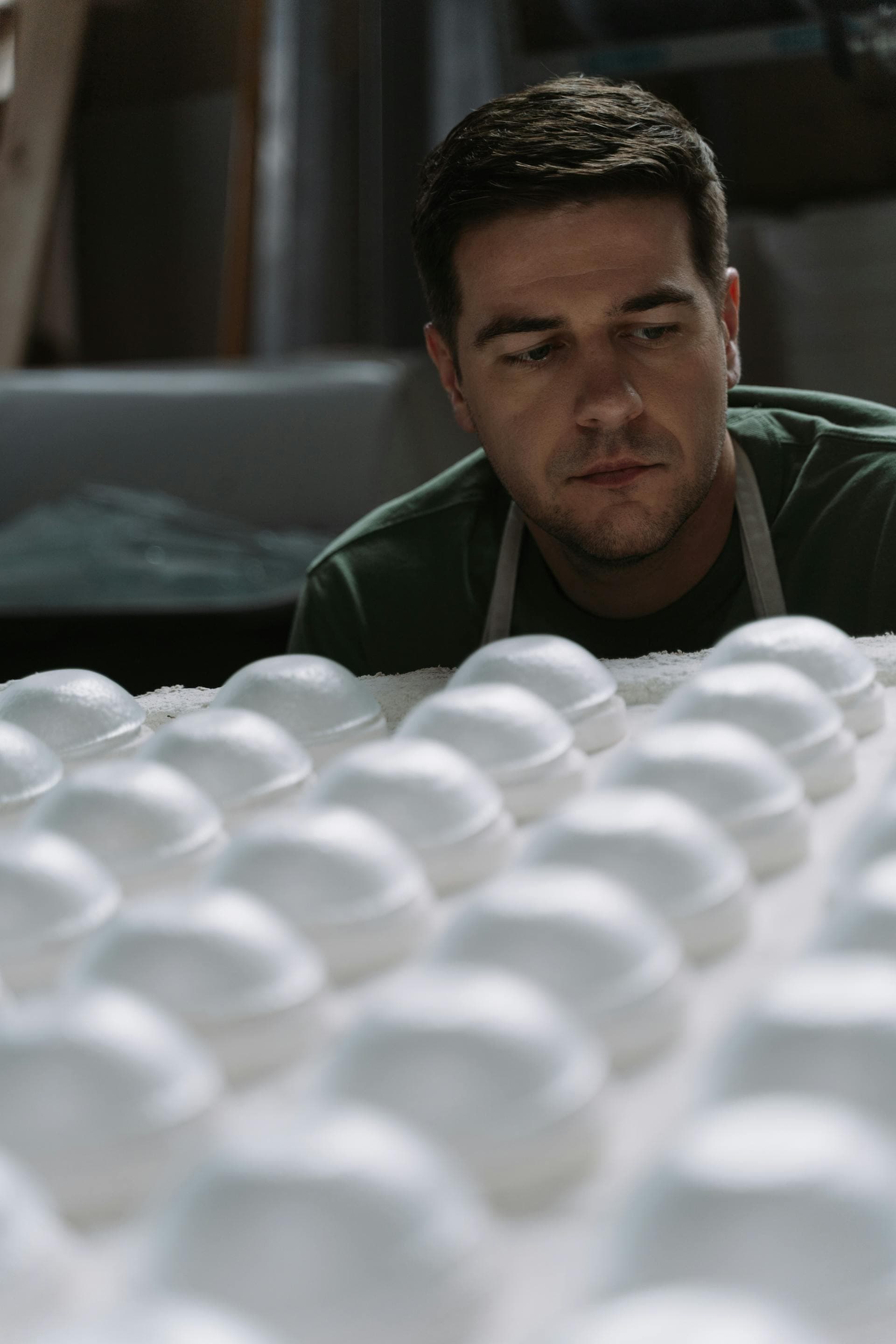 A craftsman carefully examines rows of ceramic bowls in a workshop setting